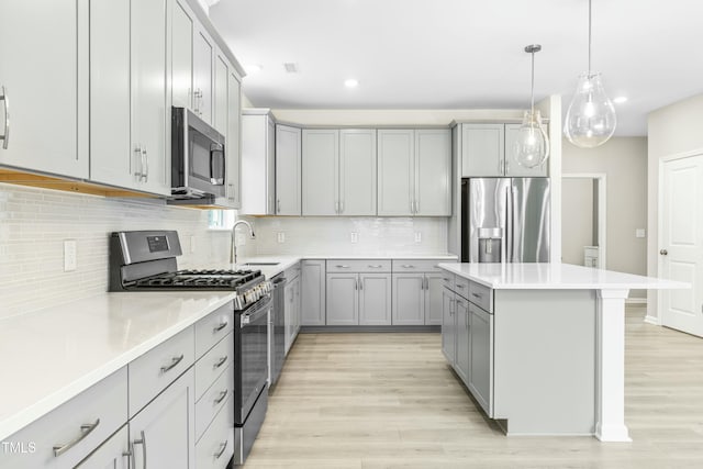 kitchen with a kitchen island, appliances with stainless steel finishes, pendant lighting, gray cabinetry, and light wood-type flooring