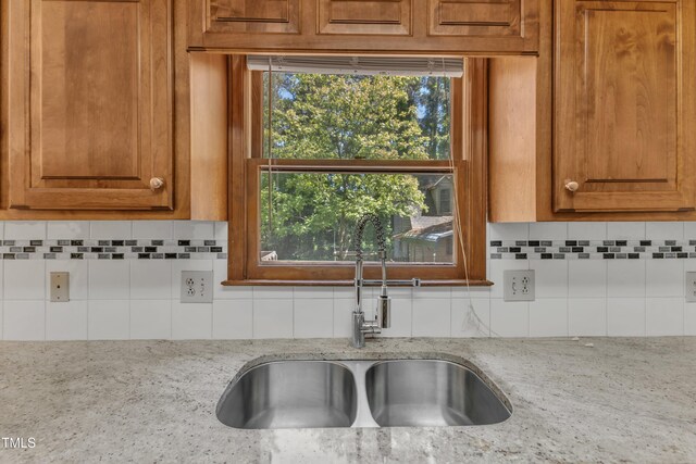 room details featuring a sink, tasteful backsplash, and light stone countertops