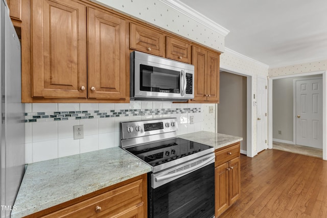 kitchen with backsplash, brown cabinets, appliances with stainless steel finishes, and ornamental molding