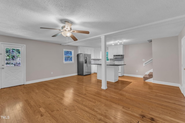 unfurnished living room with plenty of natural light, a ceiling fan, a textured ceiling, baseboards, and stairs