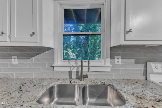 kitchen with a sink, white cabinets, light stone countertops, and tasteful backsplash