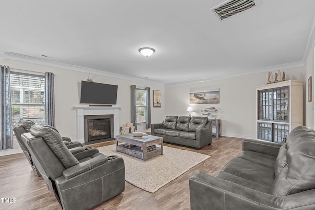 living room featuring visible vents, ornamental molding, wood finished floors, and a glass covered fireplace