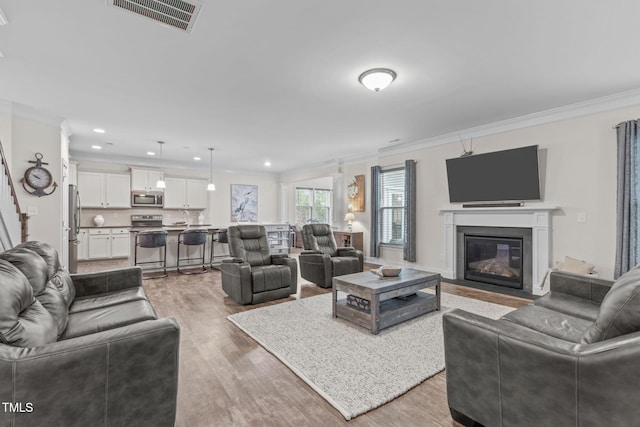 living area with a fireplace with flush hearth, visible vents, ornamental molding, and wood finished floors