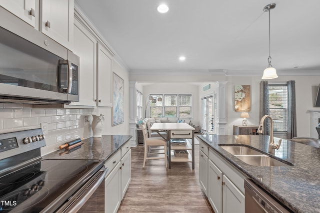 kitchen featuring a sink, white cabinetry, appliances with stainless steel finishes, dark stone countertops, and decorative light fixtures