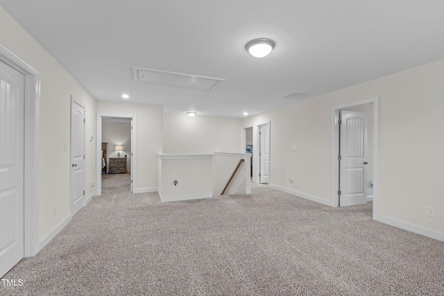 empty room featuring attic access, light colored carpet, visible vents, and baseboards