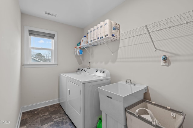 washroom with laundry area, visible vents, baseboards, washing machine and dryer, and a sink