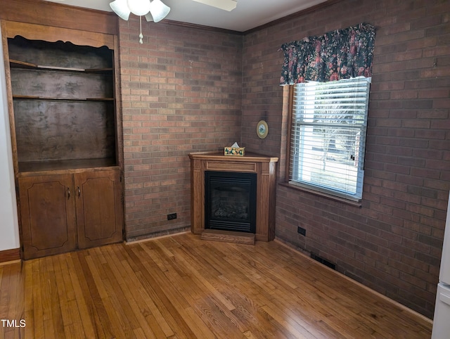 unfurnished living room featuring ceiling fan, brick wall, and light wood-type flooring