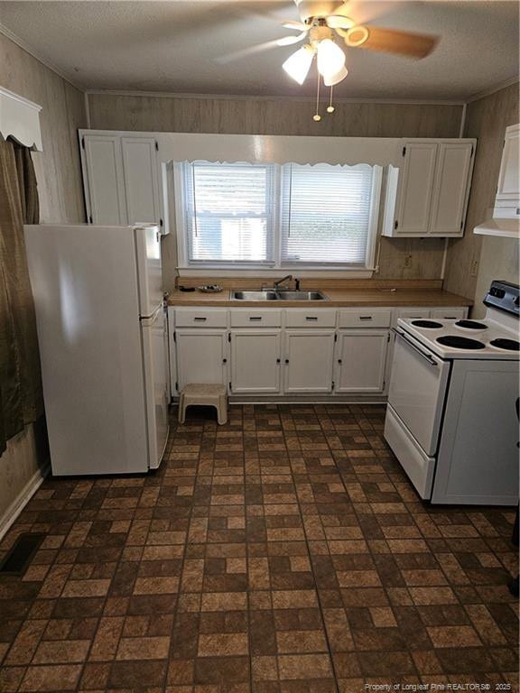 kitchen with sink, white appliances, wooden walls, ceiling fan, and white cabinets