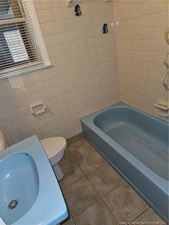 bathroom with tiled shower / bath, toilet, tile patterned flooring, and tile walls