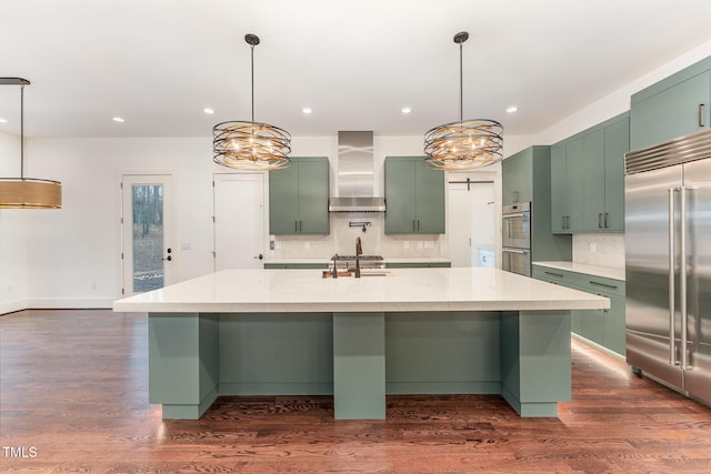 kitchen with wall chimney range hood, an island with sink, stainless steel appliances, and light stone countertops