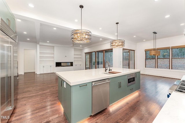 kitchen with built in appliances, hanging light fixtures, an island with sink, dark hardwood / wood-style flooring, and sink