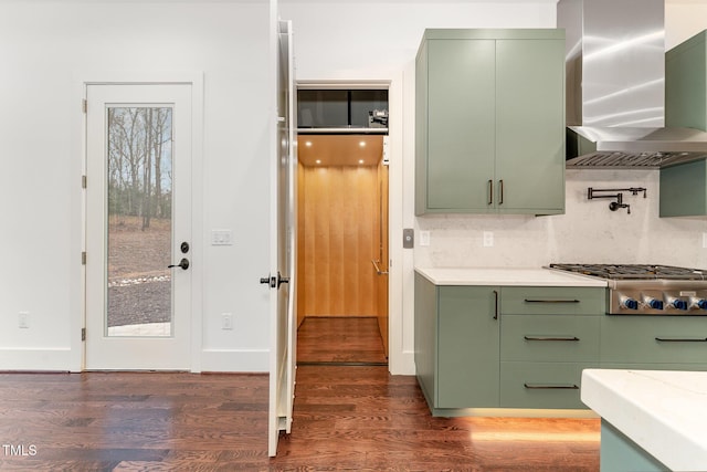 kitchen with wall chimney range hood, dark wood-type flooring, stainless steel gas cooktop, and green cabinetry