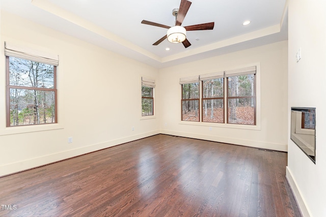 unfurnished room featuring a tray ceiling, ceiling fan, and dark hardwood / wood-style flooring