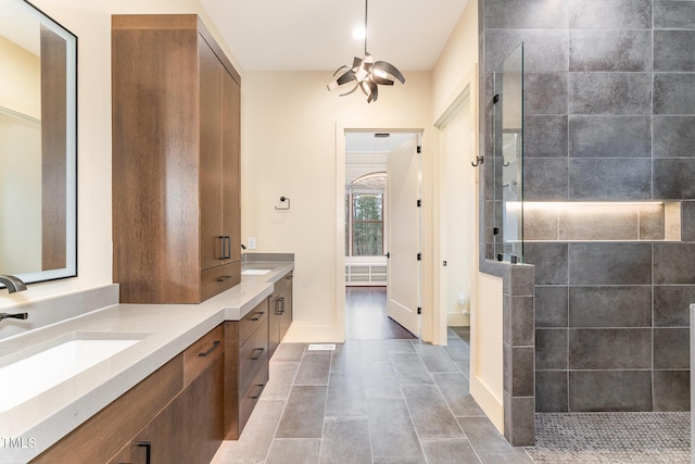 bathroom with a notable chandelier, a tile shower, and vanity