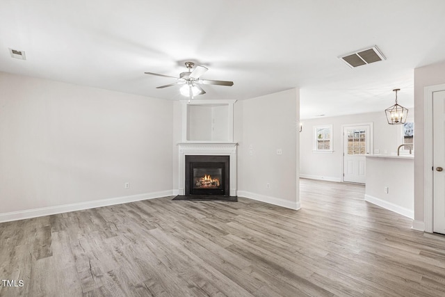 unfurnished living room with ceiling fan with notable chandelier, sink, and light hardwood / wood-style floors