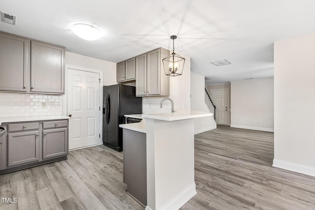 kitchen featuring hanging light fixtures, light hardwood / wood-style flooring, black refrigerator with ice dispenser, and kitchen peninsula