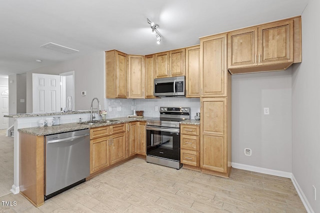 kitchen featuring sink, light stone counters, light wood-type flooring, appliances with stainless steel finishes, and decorative backsplash