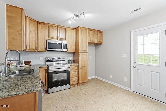 kitchen with sink, backsplash, stainless steel appliances, light stone countertops, and light hardwood / wood-style flooring