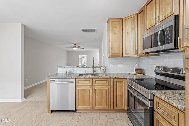 kitchen with sink, light hardwood / wood-style flooring, appliances with stainless steel finishes, backsplash, and light stone countertops