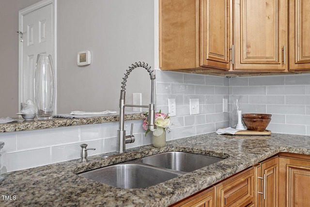 kitchen featuring tasteful backsplash, stone countertops, and sink