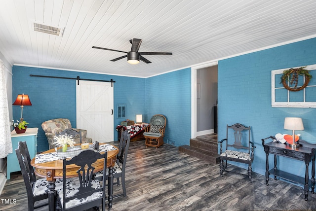 dining space with ornamental molding, dark hardwood / wood-style flooring, ceiling fan, brick wall, and a barn door