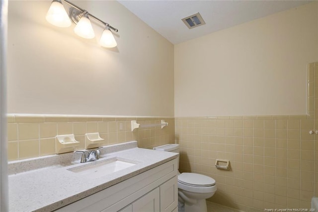 bathroom with vanity, toilet, and tile walls