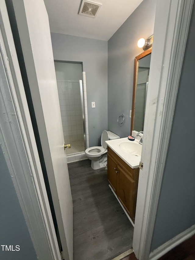 bathroom featuring a tile shower, hardwood / wood-style floors, vanity, and toilet