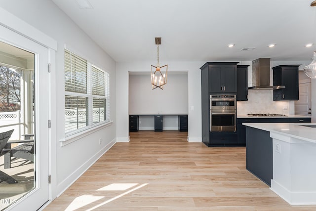 kitchen featuring decorative light fixtures, backsplash, stainless steel appliances, wall chimney range hood, and light hardwood / wood-style flooring