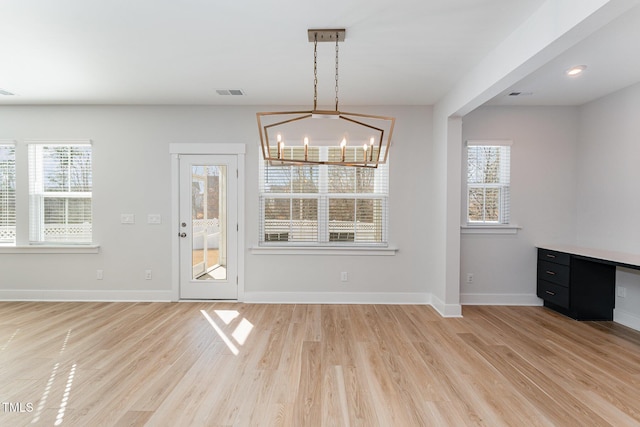 unfurnished dining area with a notable chandelier and light hardwood / wood-style flooring