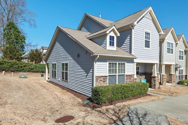 view of side of home with stone siding and a shingled roof