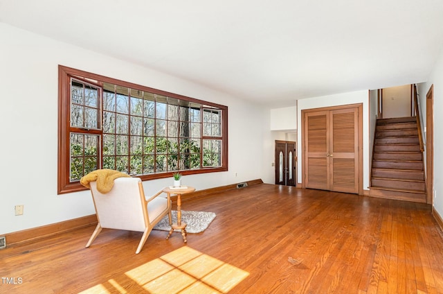 living area with visible vents, stairway, wood finished floors, and baseboards