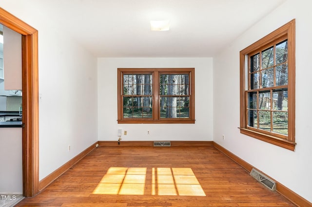 unfurnished dining area with visible vents, plenty of natural light, and wood finished floors