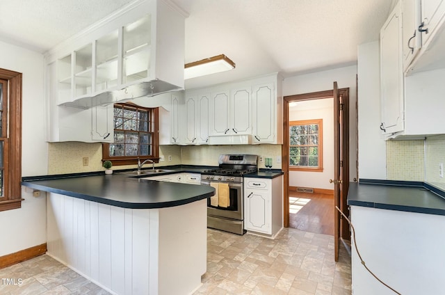 kitchen featuring dark countertops, a peninsula, stainless steel gas range, and a sink