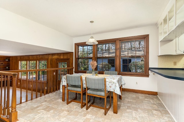 dining space featuring wooden walls, plenty of natural light, baseboards, and stone finish floor