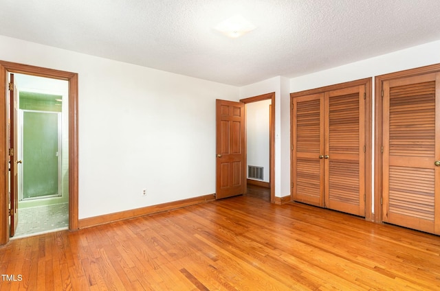 unfurnished bedroom featuring visible vents, two closets, light wood-style flooring, connected bathroom, and baseboards