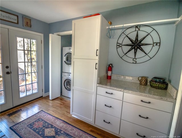 washroom with french doors, a healthy amount of sunlight, stacked washer / dryer, and light hardwood / wood-style floors