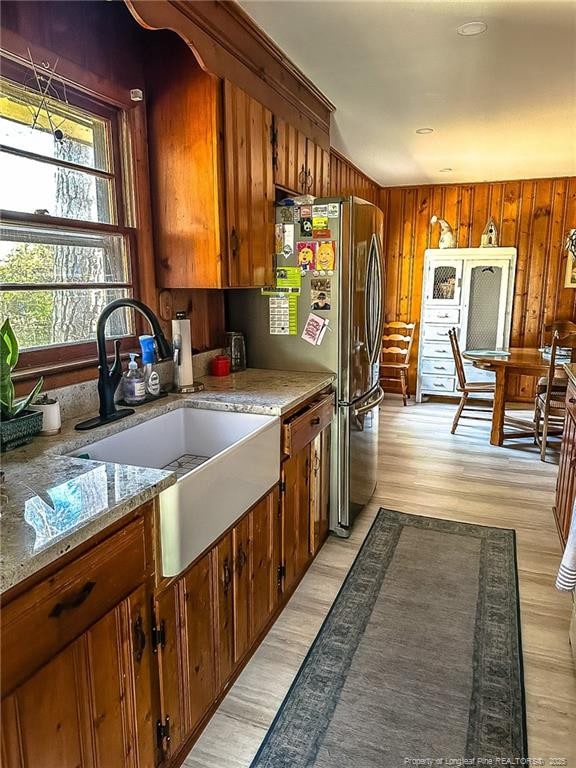 kitchen with sink, wooden walls, light hardwood / wood-style floors, and light stone countertops