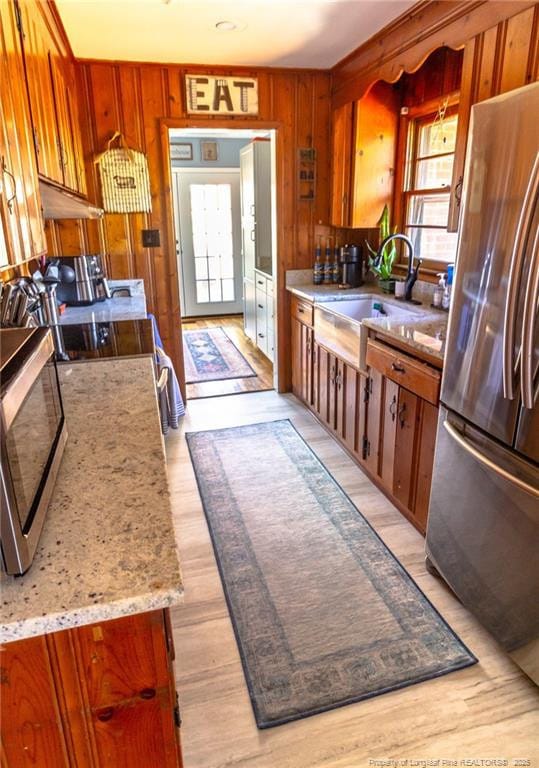 kitchen featuring stainless steel refrigerator, wood walls, sink, stove, and light hardwood / wood-style flooring