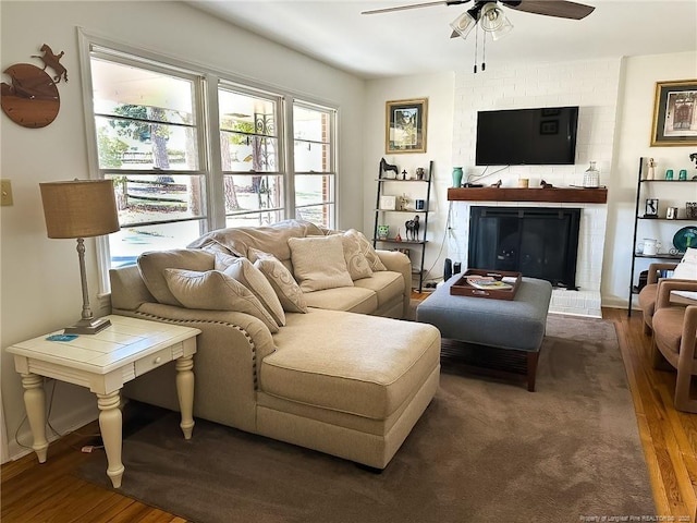 living room with a brick fireplace, dark wood-type flooring, and ceiling fan