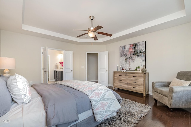 bedroom with ceiling fan, connected bathroom, dark hardwood / wood-style flooring, and a raised ceiling