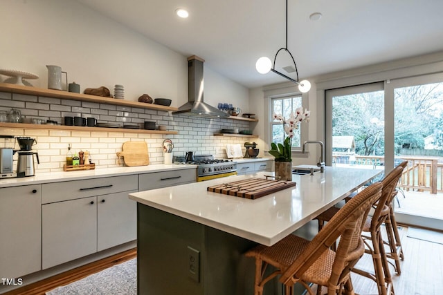 kitchen featuring wall chimney exhaust hood, decorative light fixtures, a kitchen island with sink, and white cabinets