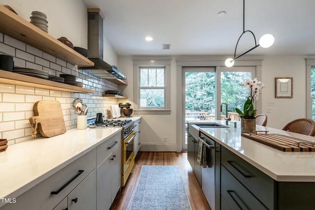 kitchen with appliances with stainless steel finishes, sink, backsplash, hanging light fixtures, and wall chimney range hood