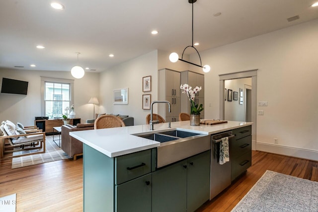 kitchen with pendant lighting, sink, stainless steel dishwasher, light hardwood / wood-style floors, and a center island with sink