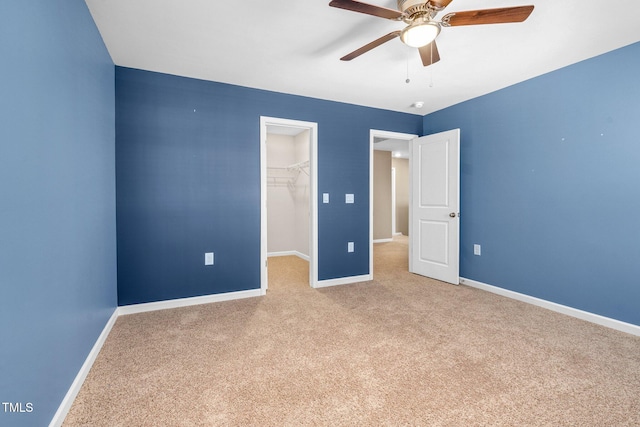 unfurnished bedroom featuring a walk in closet, light carpet, ceiling fan, and a closet