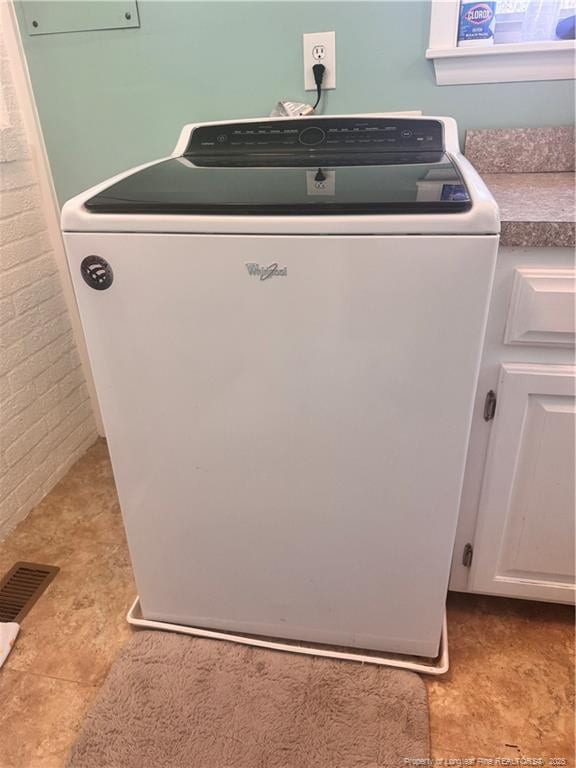 laundry area featuring washer / clothes dryer, cabinets, and brick wall