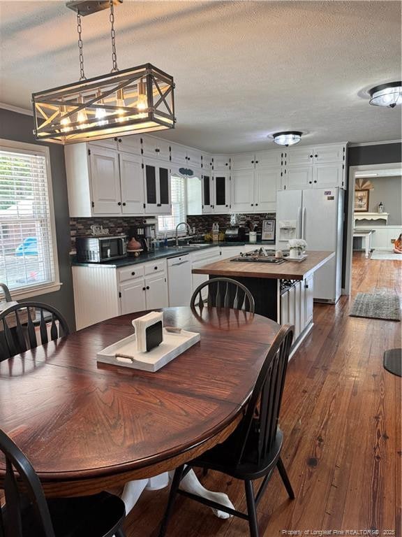 dining area featuring dark wood-type flooring, crown molding, sink, and a textured ceiling