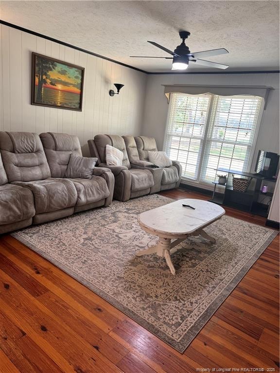 living room with wood-type flooring, ornamental molding, ceiling fan, and a textured ceiling