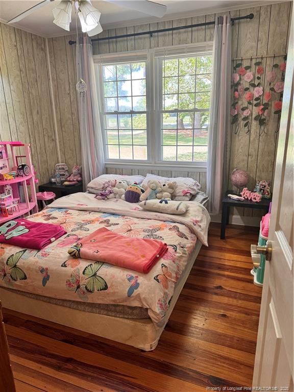 bedroom featuring ceiling fan, wooden walls, and dark hardwood / wood-style flooring