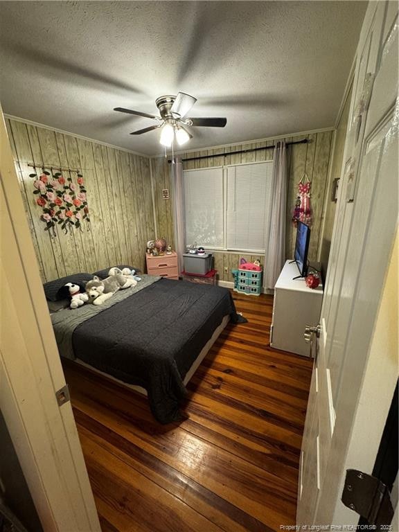 bedroom featuring ceiling fan, dark wood-type flooring, wooden walls, and a textured ceiling