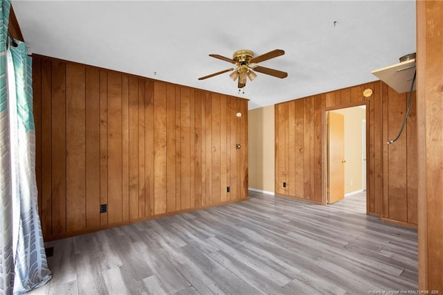 spare room featuring wood walls, ceiling fan, and light wood-type flooring